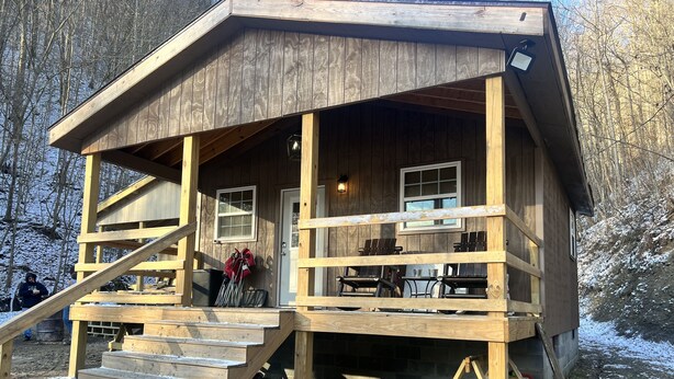 A wooden cabin with a porch, a staircase, and a window.