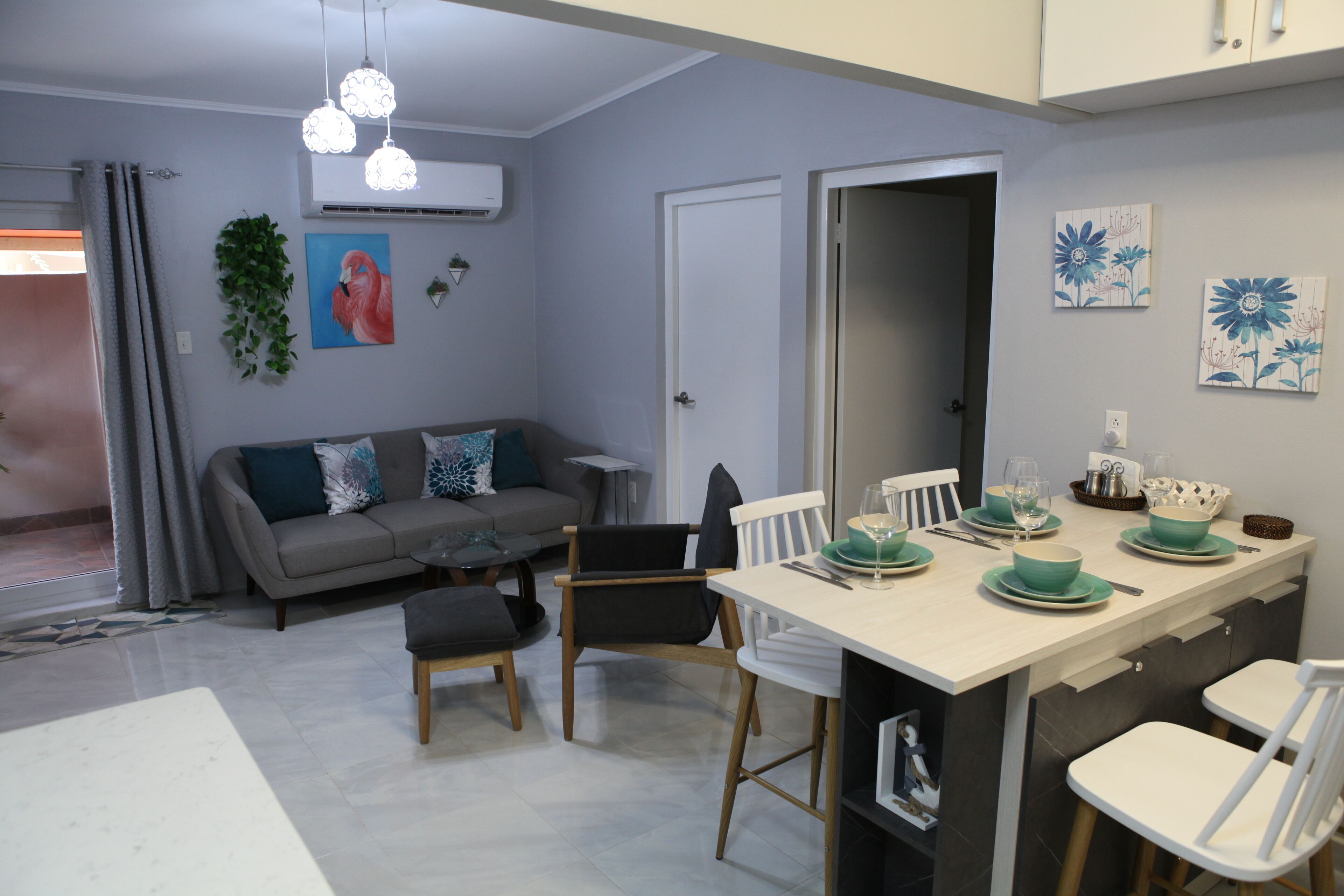 A modern kitchen with a dining area, grey walls, and a grey sofa with teal cushions.