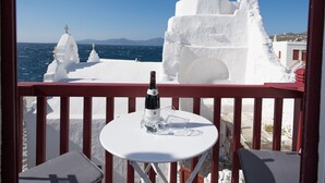 Ein Balkon mit Tisch, einer Weinflasche und Blick auf weiße Gebäude und das Meer.