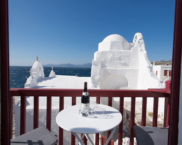 A balcony with a table, a bottle of wine, and a view of white buildings and the sea.