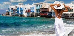 A coastal scene with white buildings and a person in a white dress by the sea.