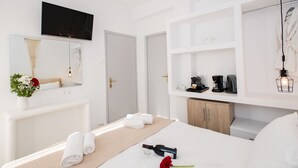 Ein modernes Hotelzimmer mit einem großen Bett, einem an der Wand befestigten Fernseher, einem Schminktisch mit Spiegel und einer Minibar.