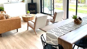 A modern living room with a large TV, a fireplace, and a dining area with a wooden table and chairs. - Lux Modern Barnhouse Cabin 1 minute from Hunter Mountain (Hunter)