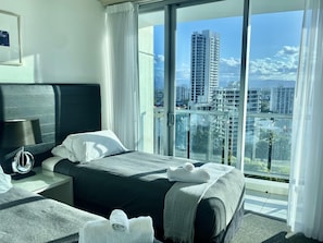 Enjoy a panoramic city view from the comfort of your room, featuring a large window, a neatly made bed, and a bedside table with a lamp.