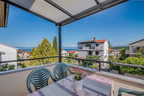 A balcony with a table and chairs, a potted plant, and a view of buildings and the sea.