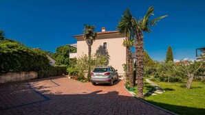 Een huis met een verharde oprit, een geparkeerde auto en een keurig onderhouden tuin met palmbomen.