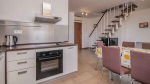 Een moderne keuken met een inbouwoven, koffiezetapparaat en een eethoek met tafel en stoelen.
