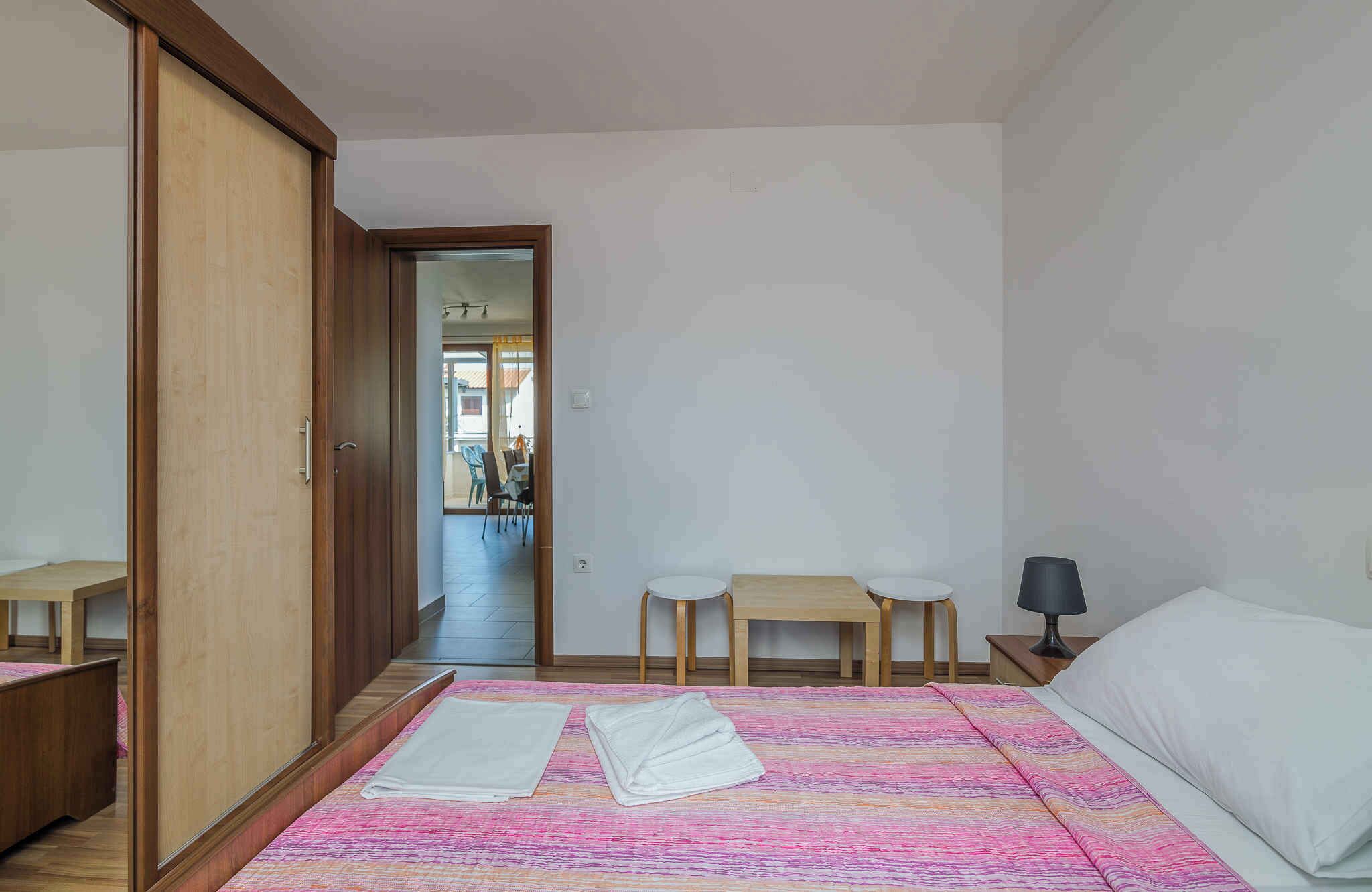 A bedroom with a bed, two bedside tables, a nightstand, a wooden wardrobe, and a view of an outdoor dining area.