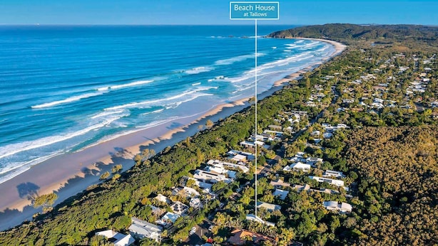 Oversigtsbillede af et kystnært boligområde med huse ud til stranden, et klart blå hav og et skilt der siger 'Beach House at Tallowes'.