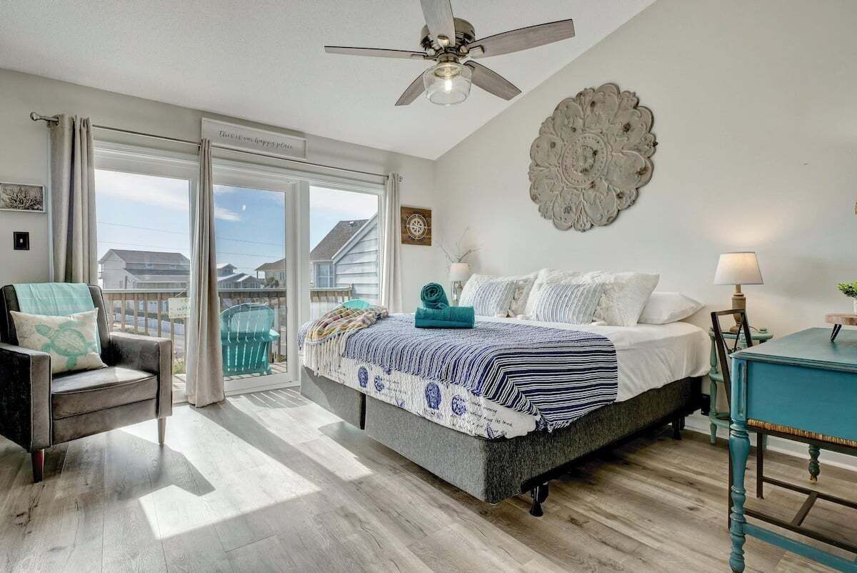 Een slaapkamer met een bed, een stoel, een tafel, een plafondventilator en uitzicht door een schuifdeur.