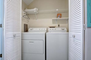 A laundry room with two white dryers and a shelf above them.