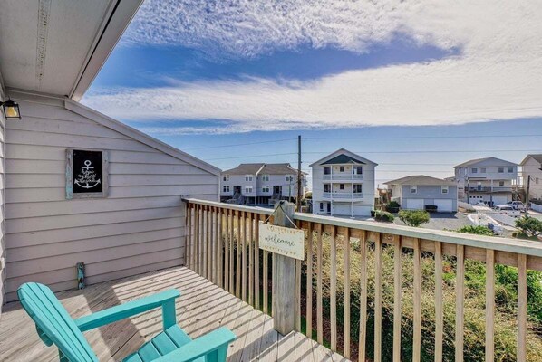 A wooden deck with a 'welcome' sign, a turquoise chair, and a view of neighboring houses.