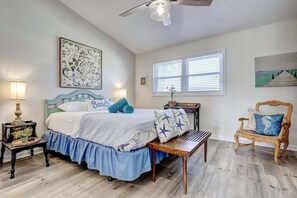 Ein Schlafzimmer mit Bett, Stuhl, Tisch, Lampe und Kunstwerken an den Wänden.