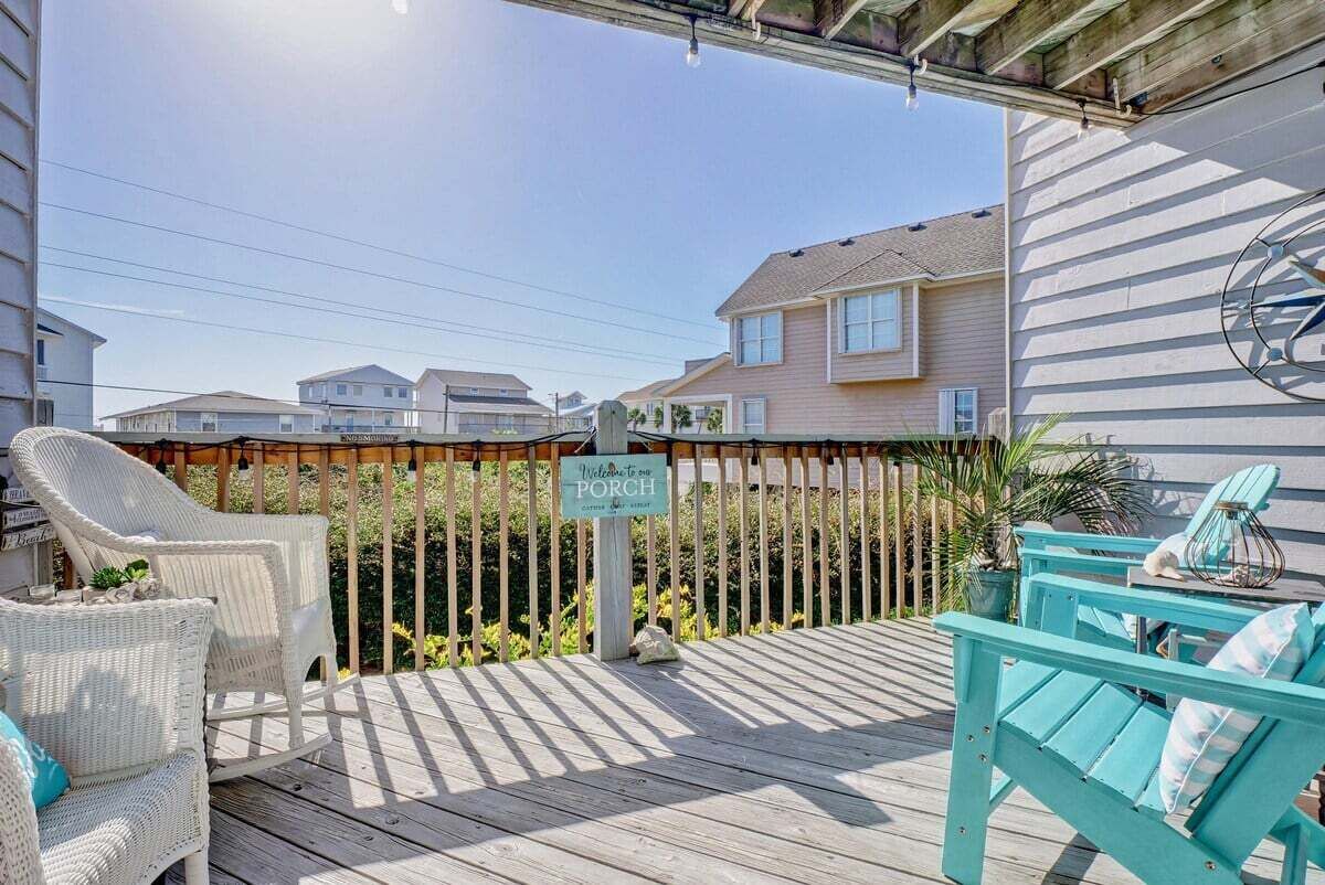 A wooden deck with outdoor furniture, a sign for a porch, and houses in the background.