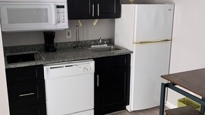 A kitchen with black and white cabinetry, a microwave, a refrigerator, a sink, and a wooden dining table.