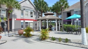 A courtyard with a gazebo, palm trees, and outdoor seating.