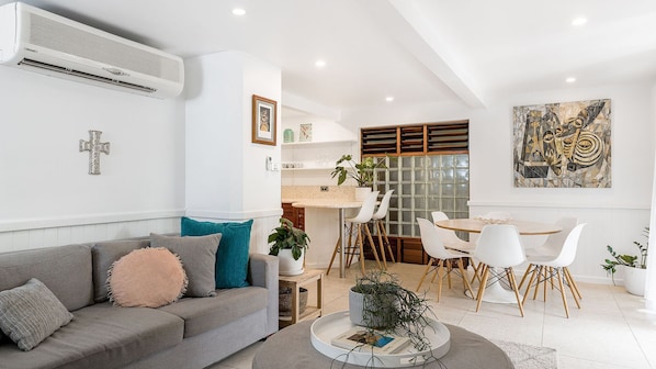 Un salon moderne avec un canapé gris, une table basse et un coin repas comprenant une table ronde et des chaises blanches.