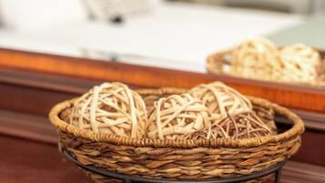 A wicker basket with a metal stand on a wooden surface, likely a table or desk, in a room with a bed in the background.