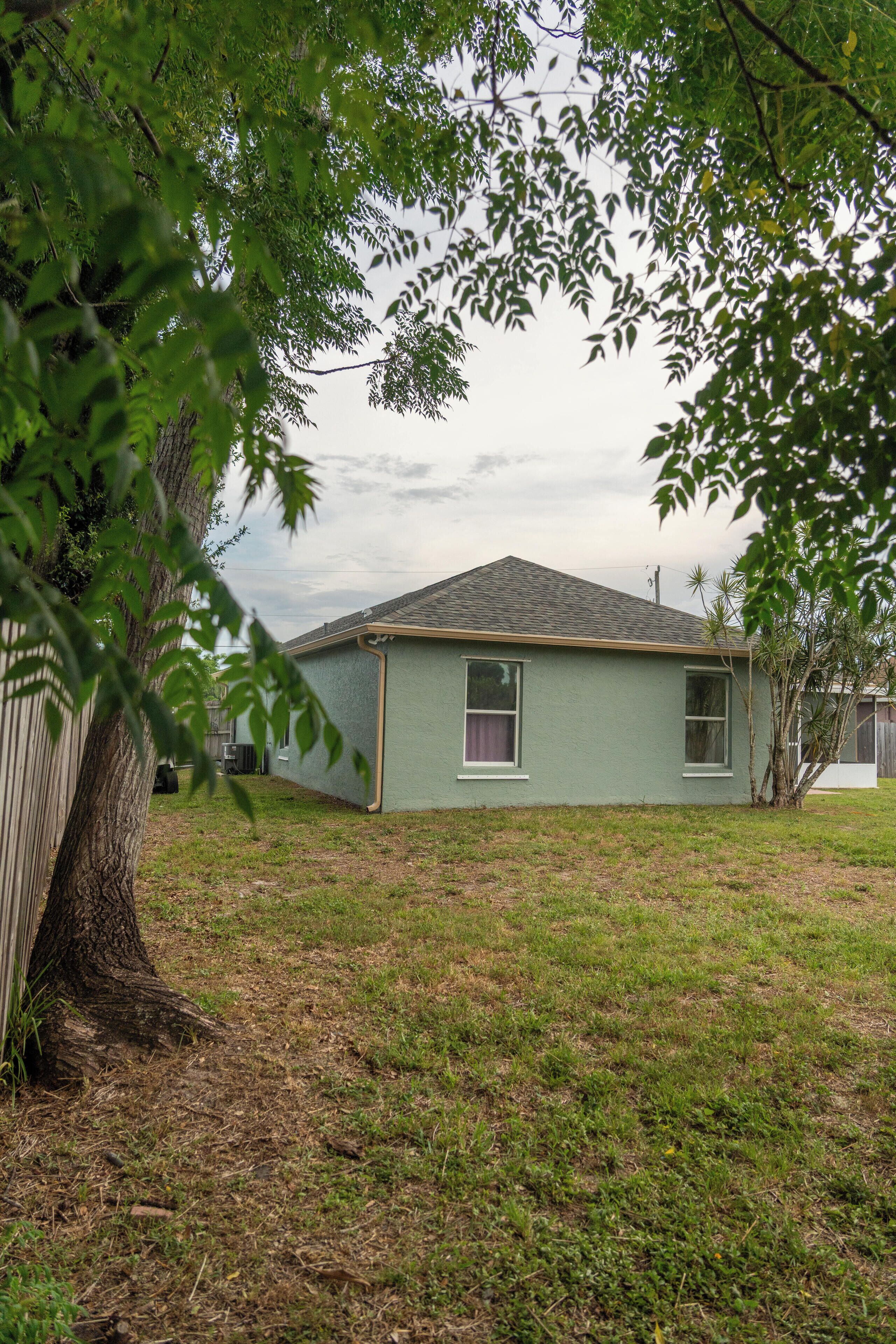 A single-story house with a sloped roof, a small front yard, and a tree in the foreground.