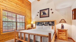 A wooden-paneled bedroom with a bed, a window with blinds, a bedside table with a lamp, and a wall-mounted picture. - Black Bear Lodge: Lovely 2BR+Loft Cedar Cabin Near Shows/Eateries/Ticket & Golf DEALS! (Branson)