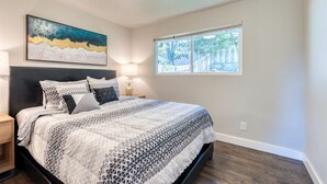 Quarto com cama, mesas de cabeceira, um quadro e janela.