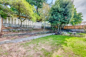 A backyard with a stone retaining wall, a wooden fence, and a grassy area with a table and chairs. - Ravishing Rambler Home! Garage / Close to Airport (SeaTac)