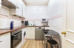 Compact kitchen with oven, dishwasher, and microwave, plus a dining area with two chairs.