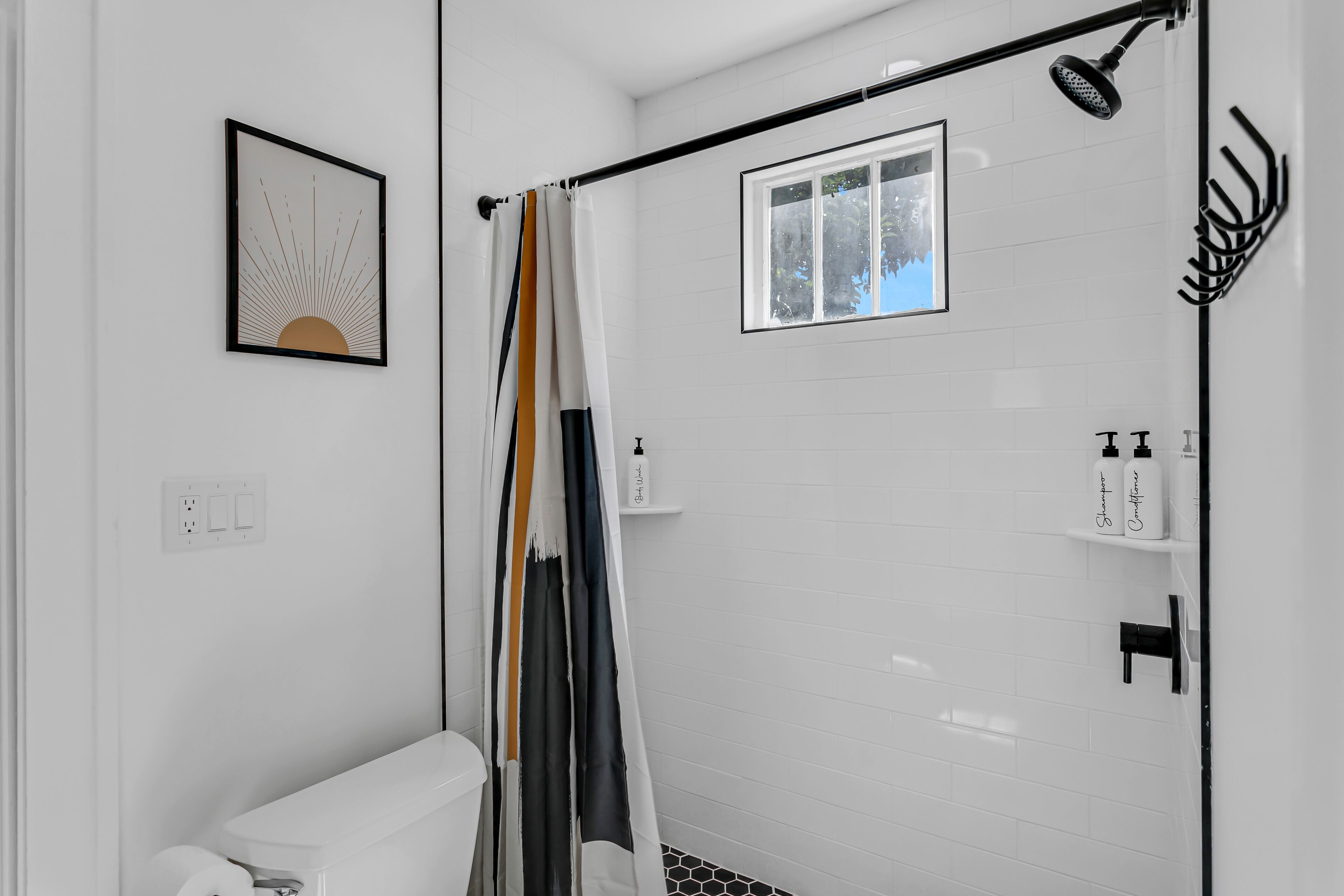 Une salle de bain moderne avec une douche, des toilettes et un lavabo. Un tableau encadré est accroché au mur et une fenêtre se trouve au-dessus de la douche.