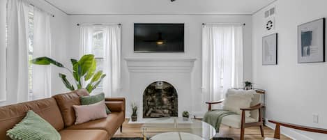 A living room with a brown leather sofa, a glass coffee table, a fireplace, and a ceiling fan.