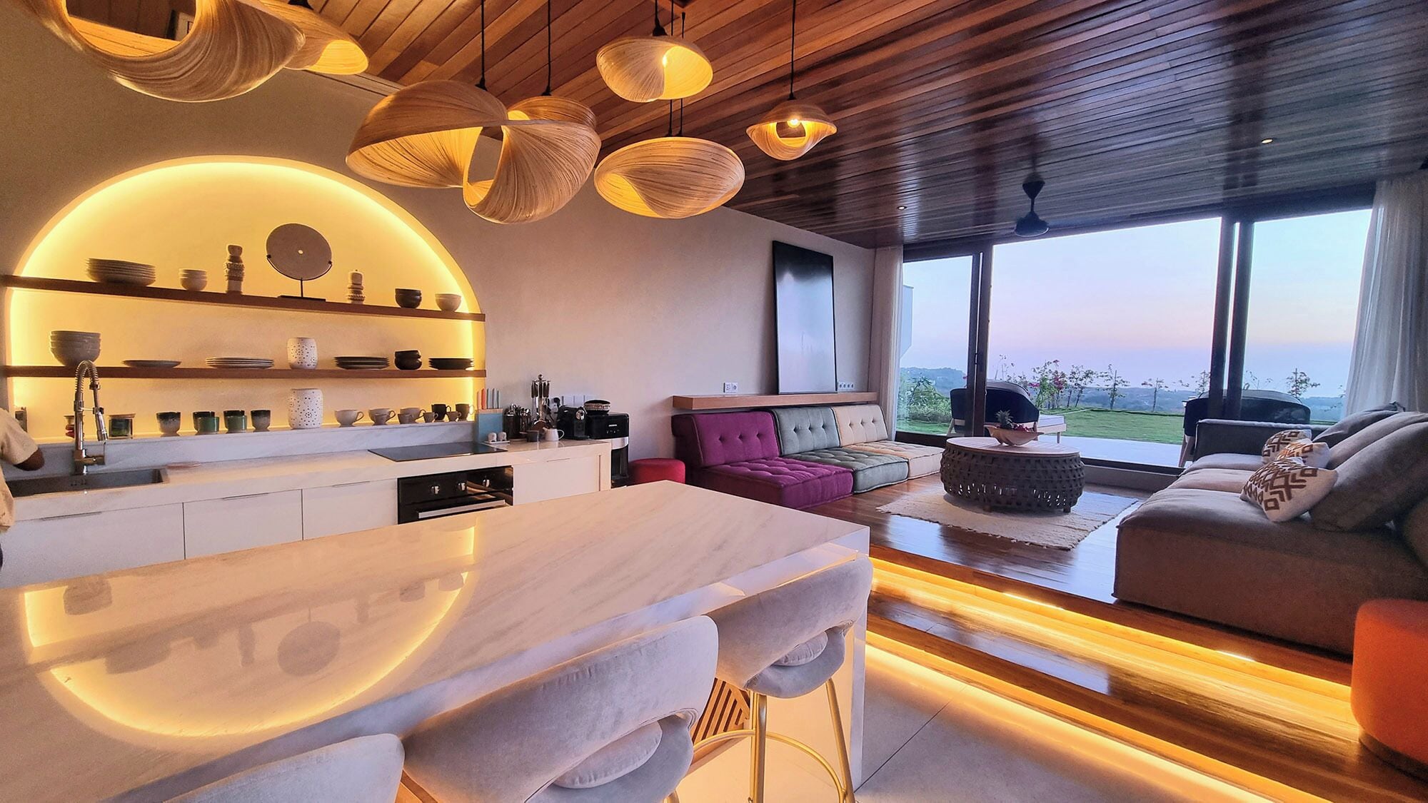 Cozinha moderna com ilha central, iluminação pendente e vista para o exterior.