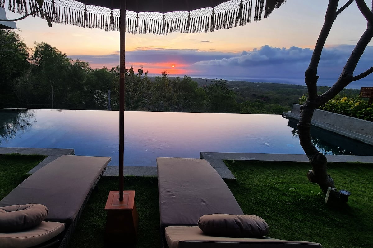 Vista del atardecer desde un área de descanso junto a la piscina, con dos tumbonas y una mesita.
