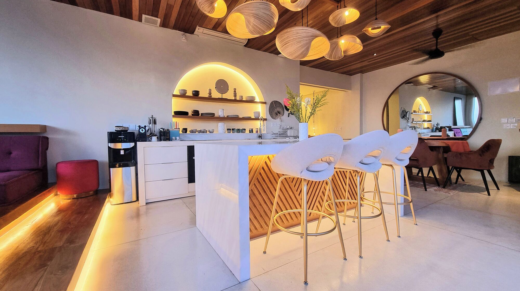 A modern kitchen with a central island, white bar stools, and pendant lighting.
