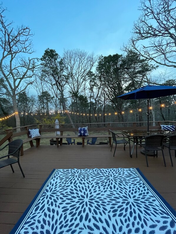 An outdoor deck with a patterned tablecloth, wooden benches, and string lights. - Spacious renovated home, close to Chatham Beaches (Harwich)