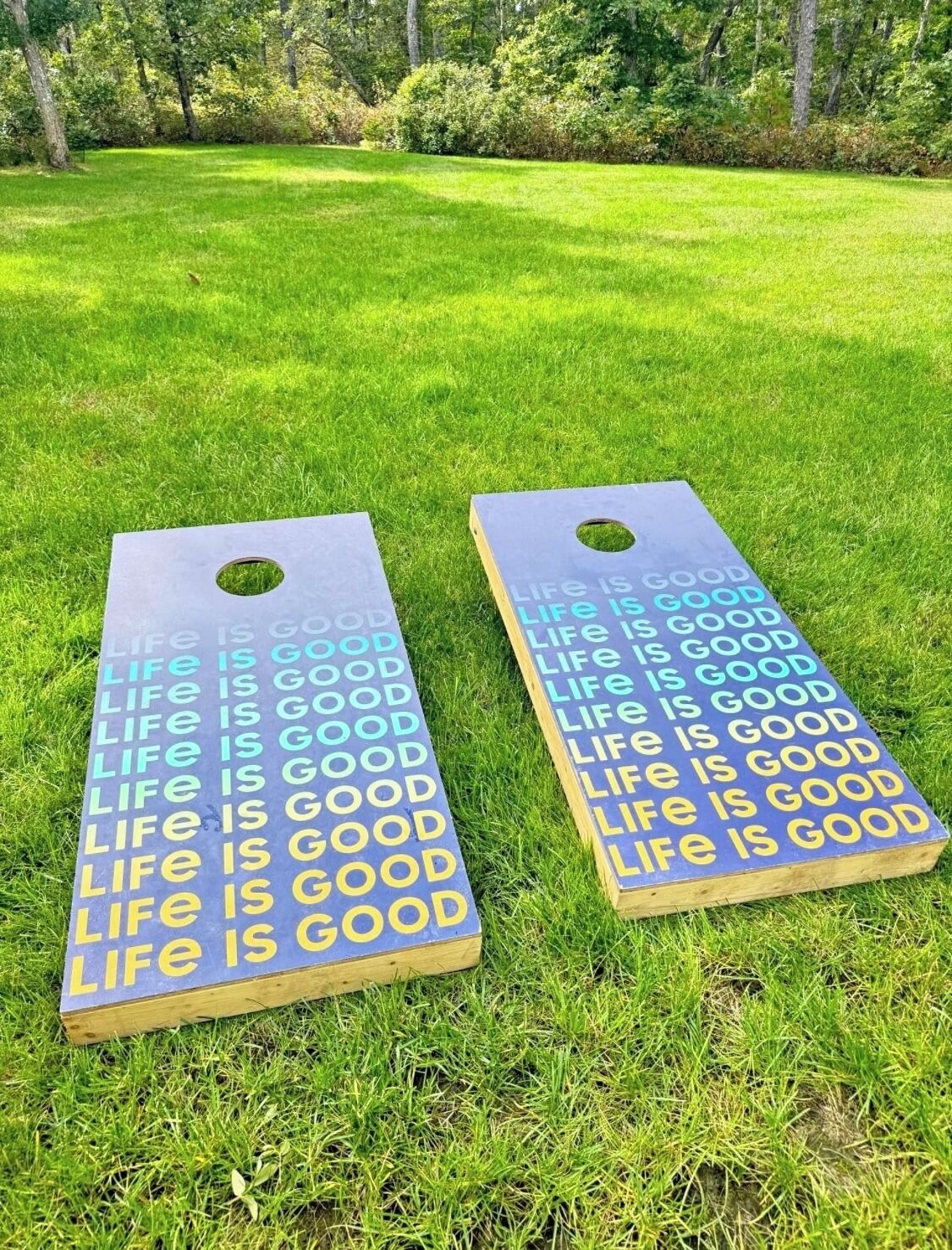 Two wooden boards with the phrase "Life is good" printed on them, placed on a grassy field.