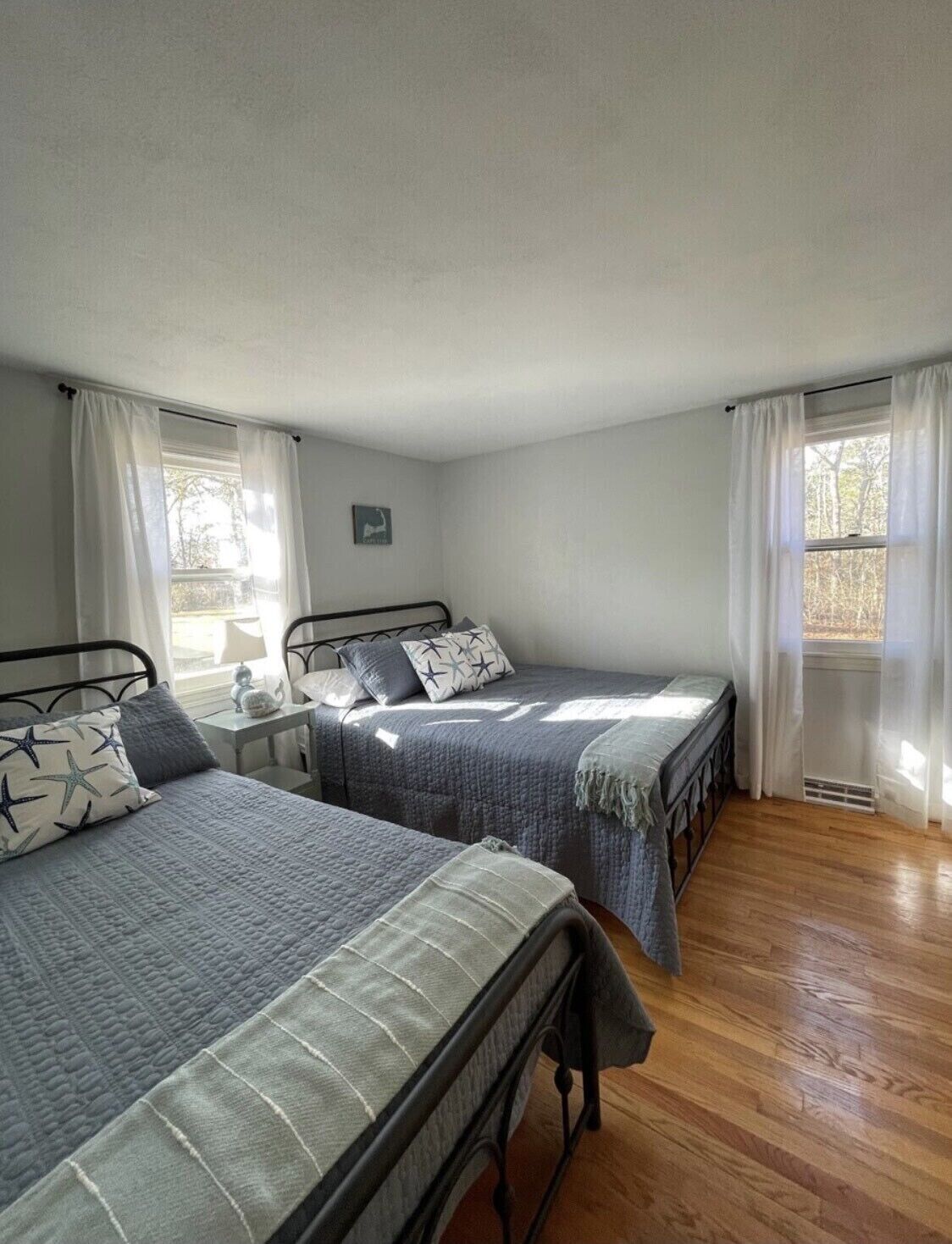 Una habitación con dos camas individuales, una mesita con lámpara y un ventanal con cortinas.
