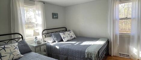 Una habitación con dos camas individuales, una mesita con lámpara y un ventanal con cortinas.