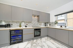 Eine moderne Küche mit grauen Schränken, einer gefliesten Spritzschutzwand, einem integrierten Weinkühler und einem Backofen.