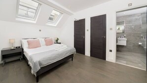 Ein Schlafzimmer mit Bett, Nachttischen, einem Oberlicht und einem Badezimmer mit Duschkabine.