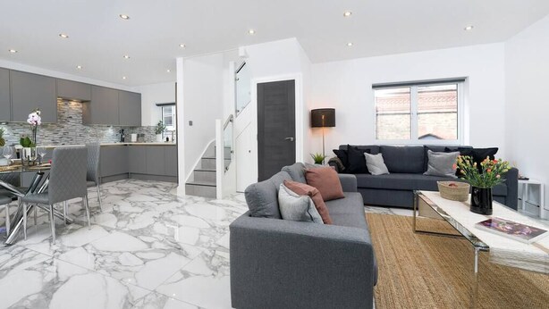 Ein modernes Wohnzimmer mit grauem Sofa, einem Essbereich mit Glastisch und einer Küche mit grauen Schränken.