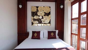 Cama com roupa de cama branca, duas almofadas com bordado dourado e uma obra de arte floral pendurada na parede.