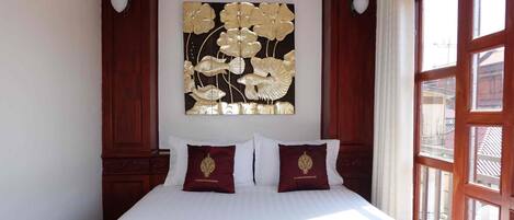 A bed with white linens, two pillows with gold embroidery, and a wall-mounted artwork of flowers.