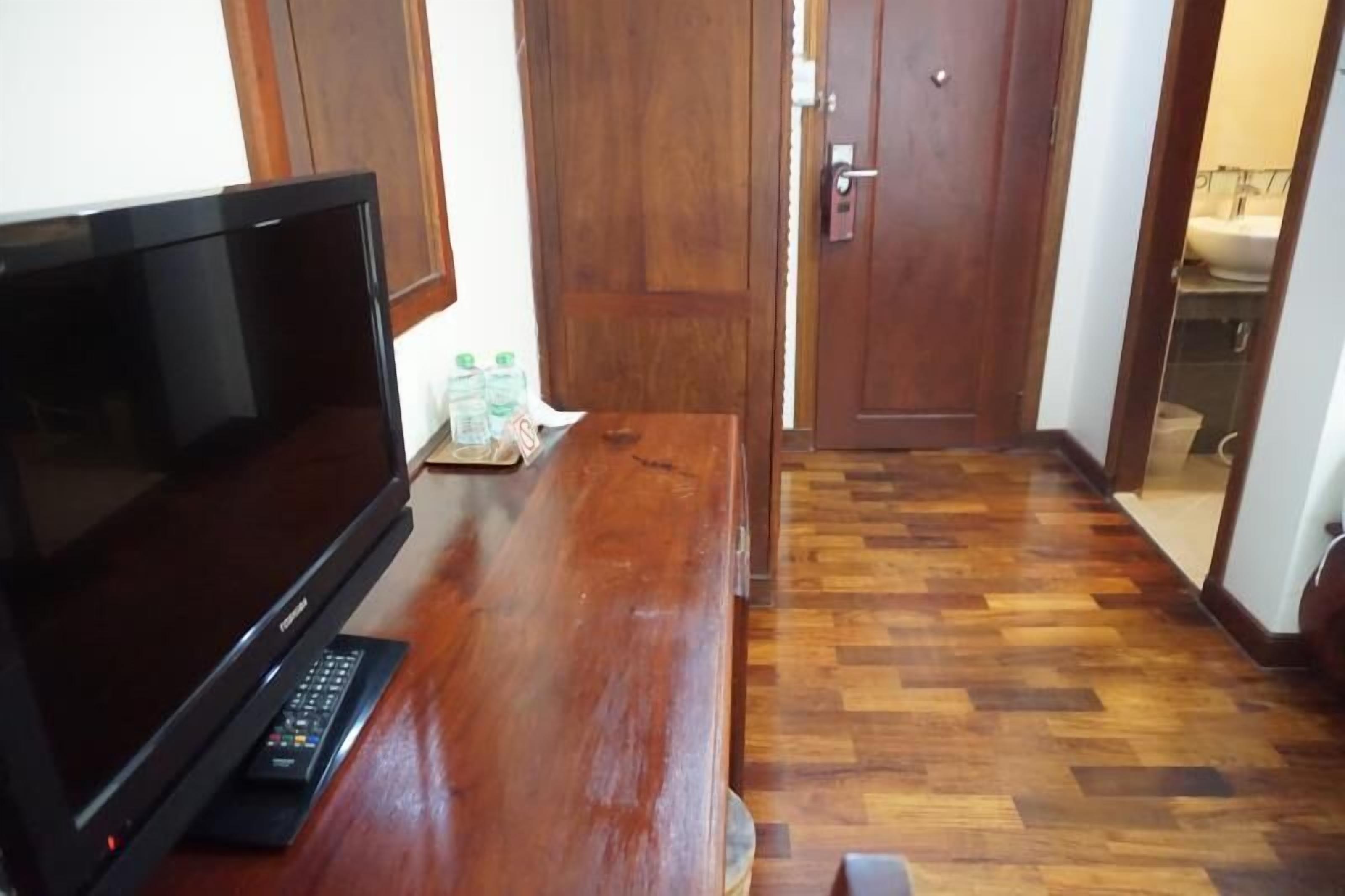 A wooden bench with a flat-screen TV and remote control, a wooden door, and a tiled floor.