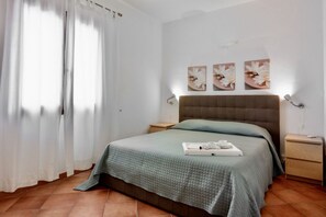 A neatly made bed with a green quilt, a bedside table with a lamp, and a wall with three floral paintings.