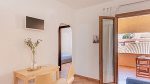 A room with a wooden desk, two chairs, a TV mounted on the wall, a large window with a view of buildings, and a sliding glass door leading to an outdoor area. - (30/45 sq m): living room with kitchenette, double sofa bed and a single folding bed, double bedroom, bathroom and balcony.<br>Features: <br>tv, <br>ironing board and iron (on request) <br>kitchenette with induction hub, <br>oven, <br>kettle, <br>microwa (Santa Teresa di Gallura)