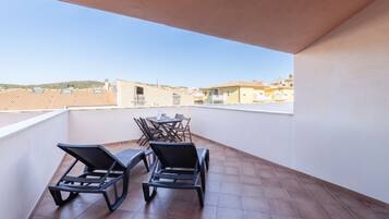A balcony with two lounge chairs and a table, overlooking a residential area with tiled roofs.