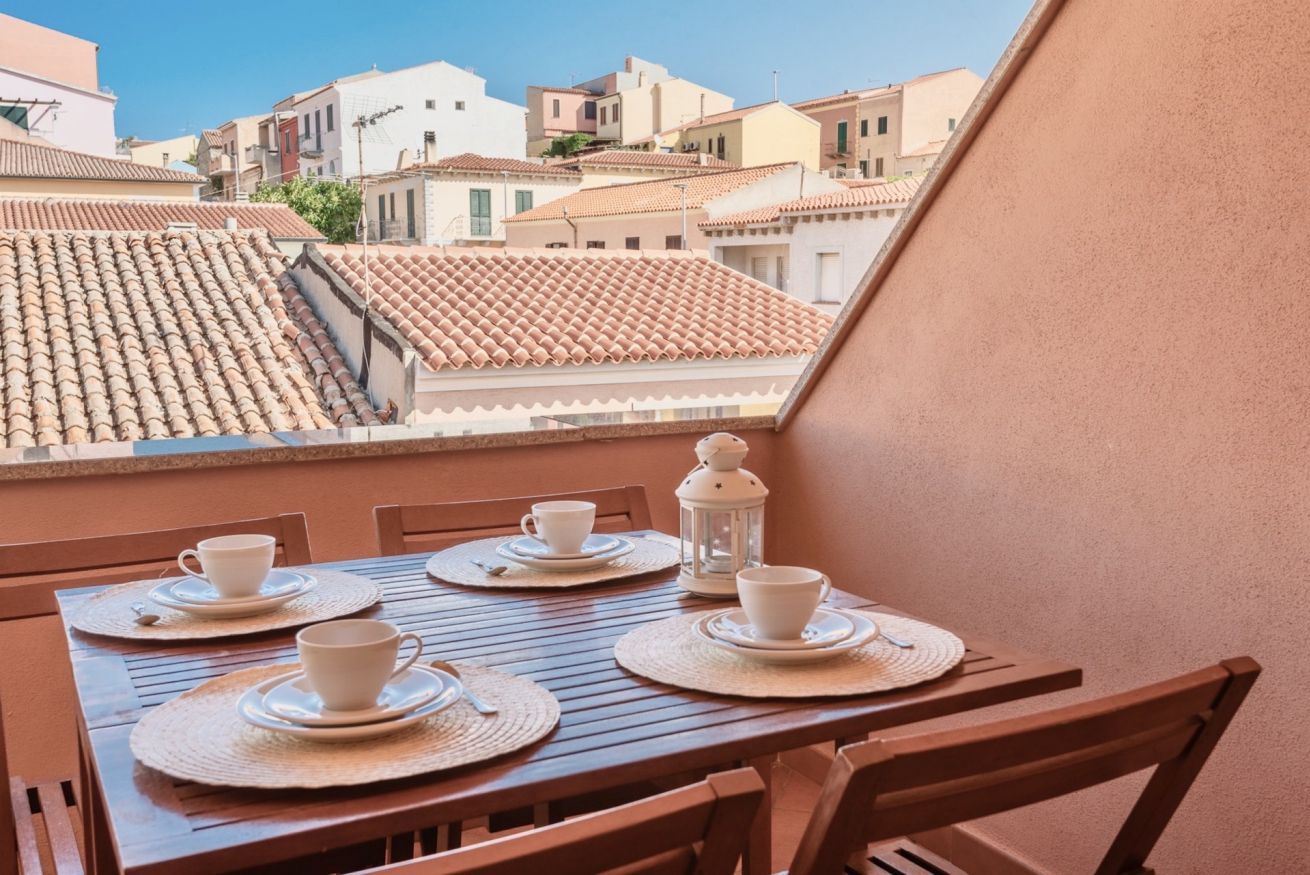 Ein Balkon mit Tisch für zwei Personen, Blick auf eine Stadtlandschaft mit Terrakotta-Dachziegeln.