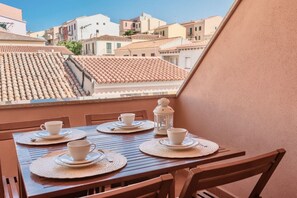 A balcony with a table set for two, overlooking a cityscape with terracotta-tiled roofs. - (30/45 sq m): living room with kitchenette, double sofa bed and a single folding bed, double bedroom, bathroom and balcony.<br>Features: <br>tv, <br>ironing board and iron (on request) <br>kitchenette with induction hub, <br>oven, <br>kettle, <br>microwa (Santa Teresa di Gallura)