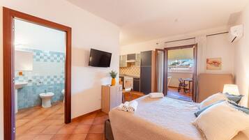Ein Hotelzimmer mit Bett, Fernseher, Bad mit Waschbecken und Toilette sowie Balkon mit Tisch und Stühlen.