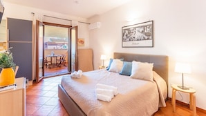 A well-lit bedroom with a large bed, a desk with a yellow vase, a chair, and a view of the outside through a sliding door. - (25/30 sq m): living room with kitchenette, double bed, double sofa bed or 2 single folding beds, bathroom, balcony.<br>Features: <br>tv, <br>ironing board and iron (on request) <br>kitchenette with induction hub, <br>oven, <br>kettle, <br>microwave <br> (Santa Teresa di Gallura)