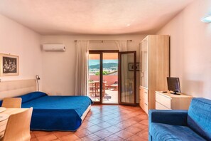 A hotel room with two beds, a TV, a desk, and a view of the outdoors.